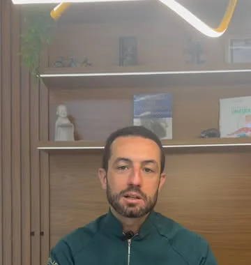 Dr. Gabriel Bruzadelli no consultório, com estante de madeira e livros ao fundo.